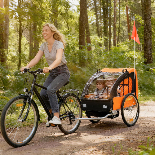 Woman riding a bicycle with a child in a trailer through a forest.
